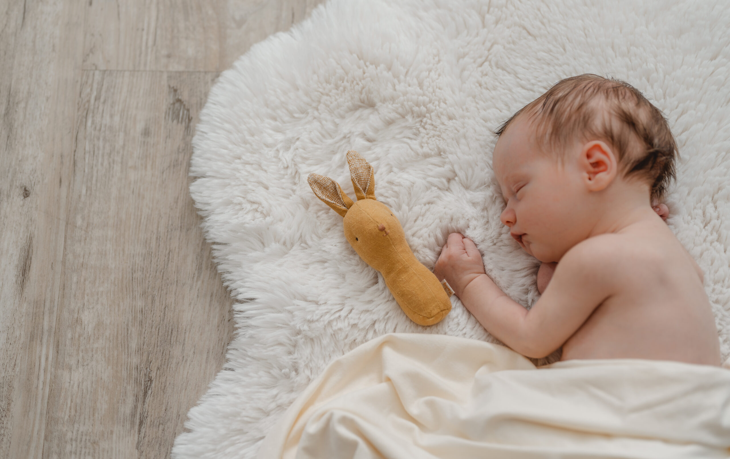 Natürliche Neugeborenenfotografie, ein entspannt schlafendes Baby in den ersten Lebenstagen auf einem weißen Fell